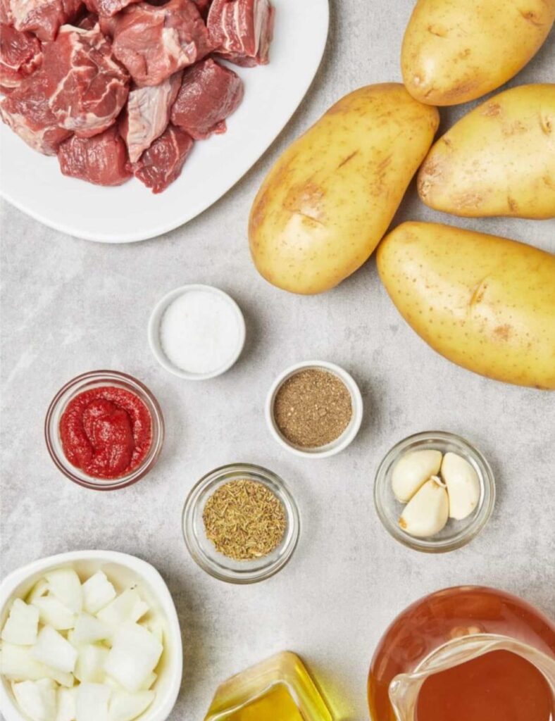 Ingredients for beef stew arranged on a table, including meat, vegetables, and seasonings.

