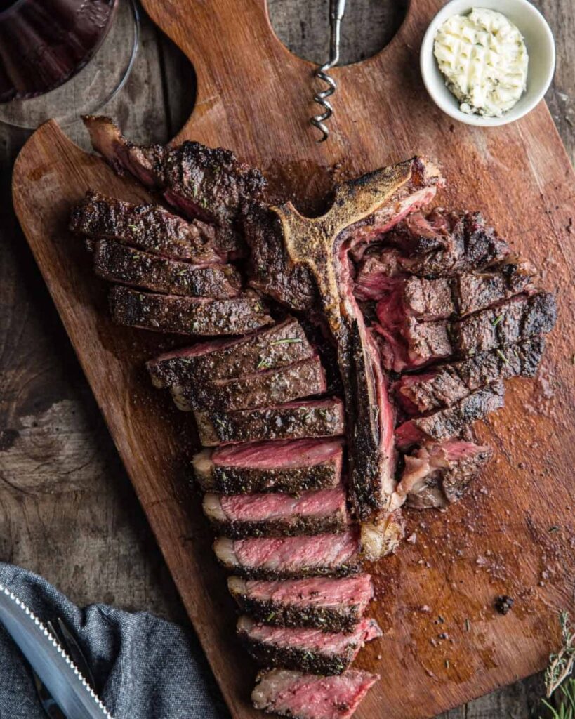 Two steaks sizzling on a grill, surrounded by vibrant flames.