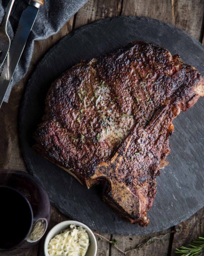 A cooked steak on a white plate, accompanied by a knife and fork placed beside it.