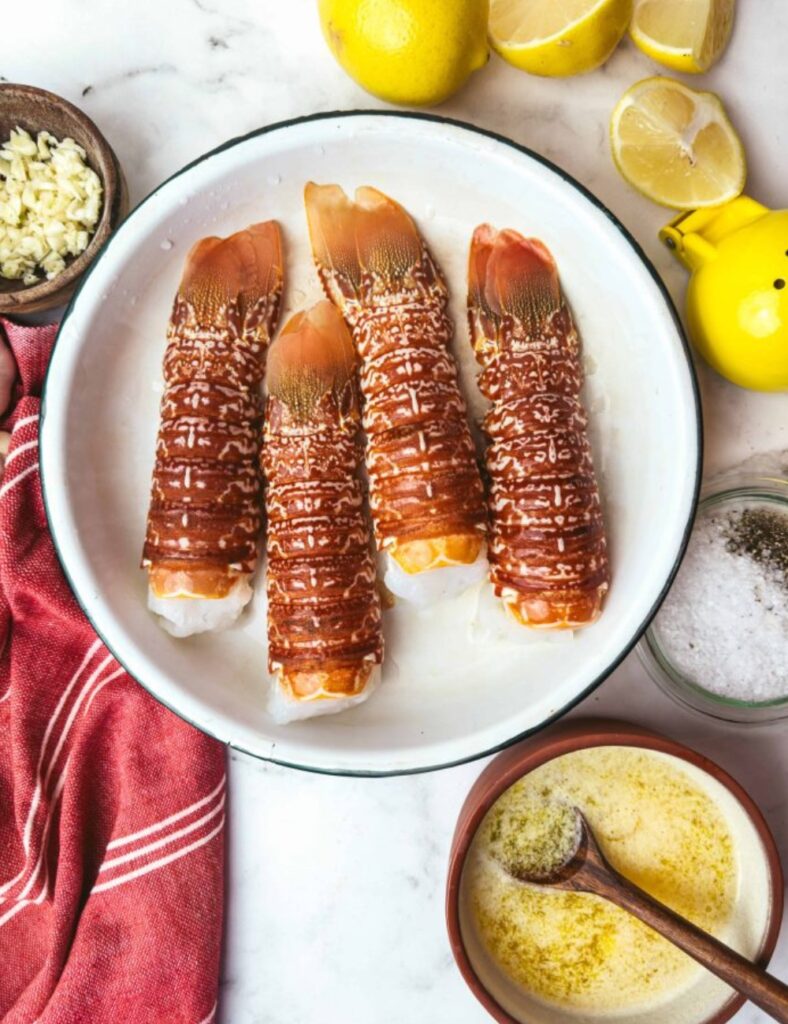 Three lobster tails arranged in a white bowl, accompanied by fresh lemon slices for garnish.