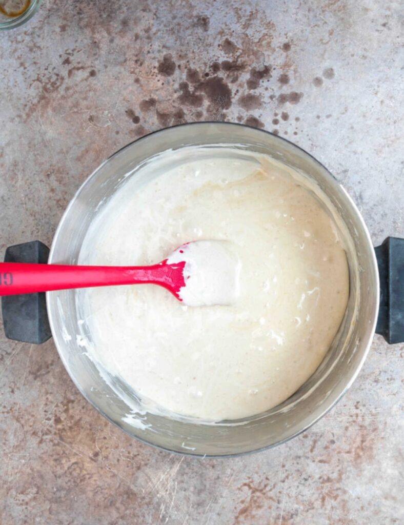 A bowl of batter sits on a countertop, with a red spatula resting inside it.

