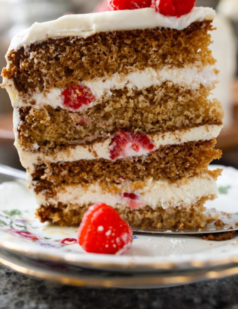A round cake topped with fresh raspberries, with a slice removed, revealing its moist interior.