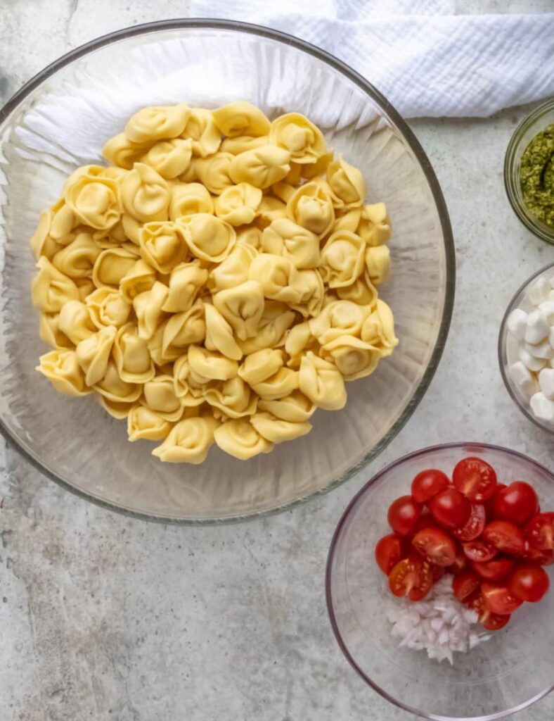 8 oz cheese tortellini
1 cup cherry tomatoes, halved
1 cup fresh spinach, chopped
1/2 cup mozzarella balls
1/4 cup pesto sauce
1/4 cup grated Parmesan cheese
Salt and pepper to taste