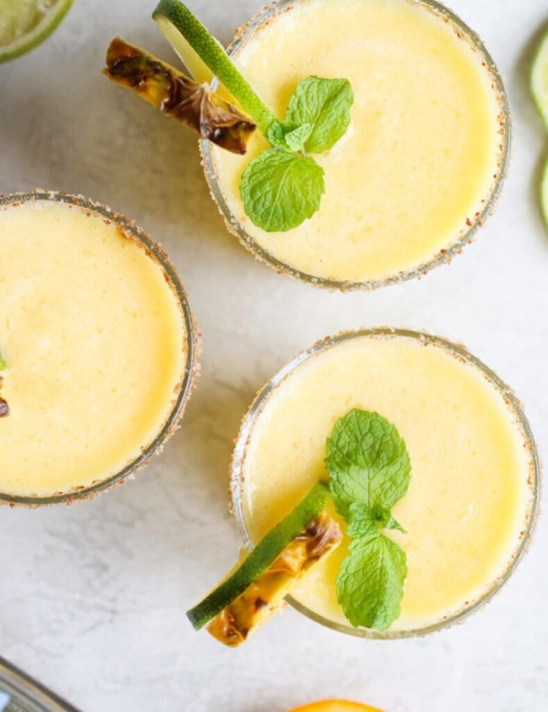 Three glasses of orange juice garnished with mint leaves and lime slices, arranged on a wooden table.