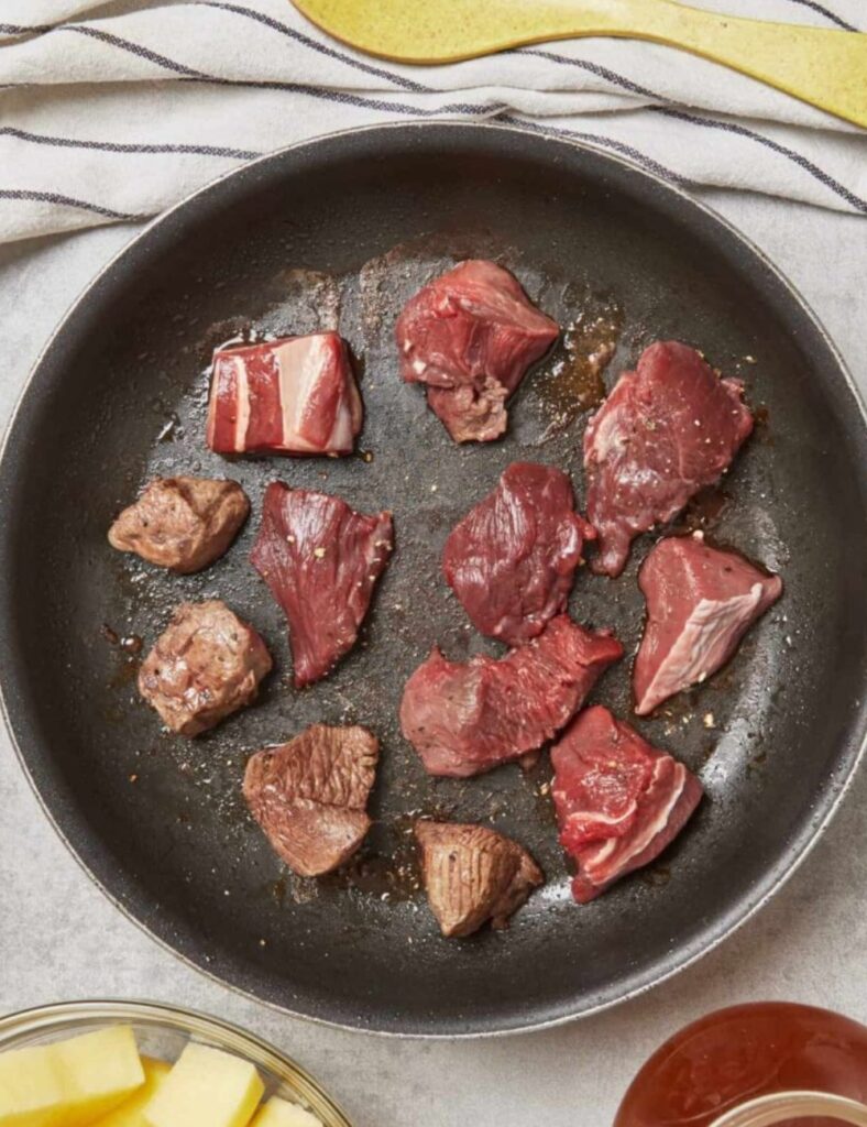 A frying pan containing raw meat and a pat of butter, ready for cooking.

