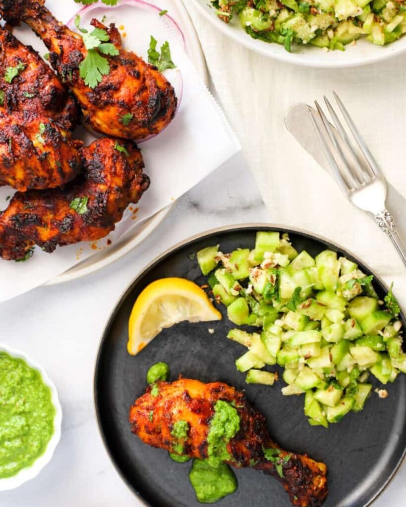Chicken tikka masala served with a side of fresh cucumber salad on a white plate.