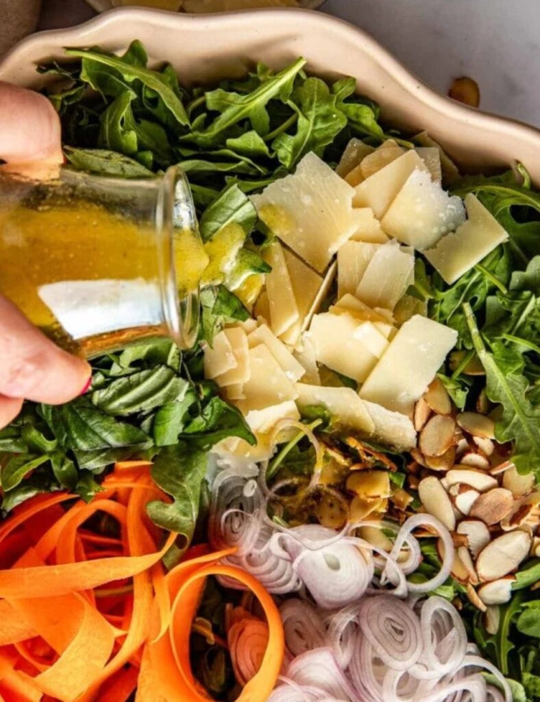 A person drizzles dressing over a colorful salad with carrots, onions, and cheese in a bowl.