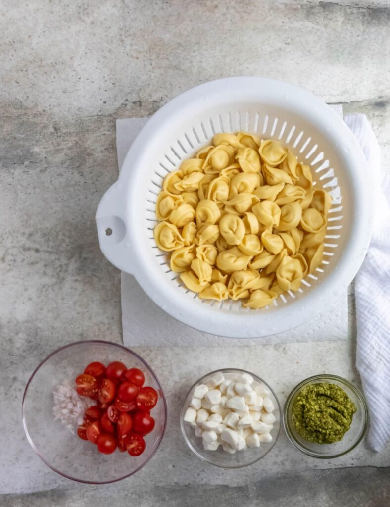 8 oz cheese tortellini
1 cup cherry tomatoes, halved
1 cup fresh spinach, chopped
1/2 cup mozzarella balls
1/4 cup pesto sauce
1/4 cup grated Parmesan cheese
Salt and pepper to taste