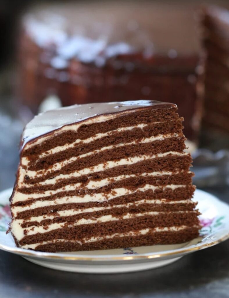 A slice of rich chocolate cake on a white plate, garnished with a dusting of cocoa powder.

