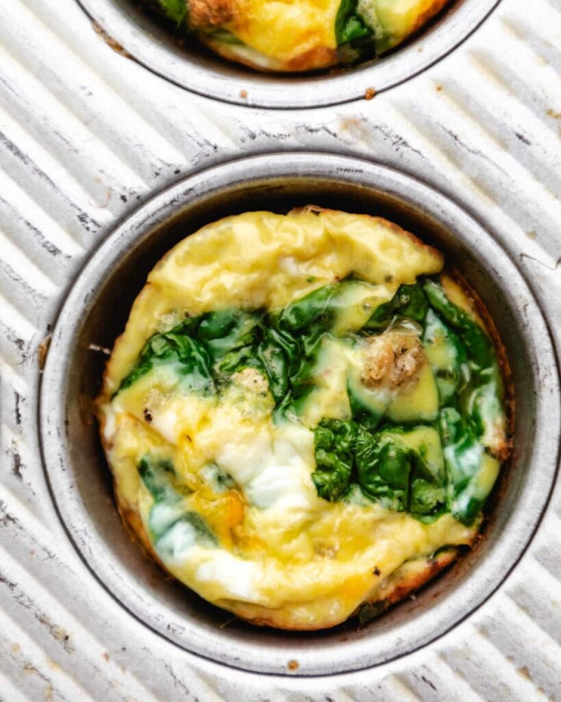 Muffin pan filled with baked egg and spinach mixture, ready for serving.