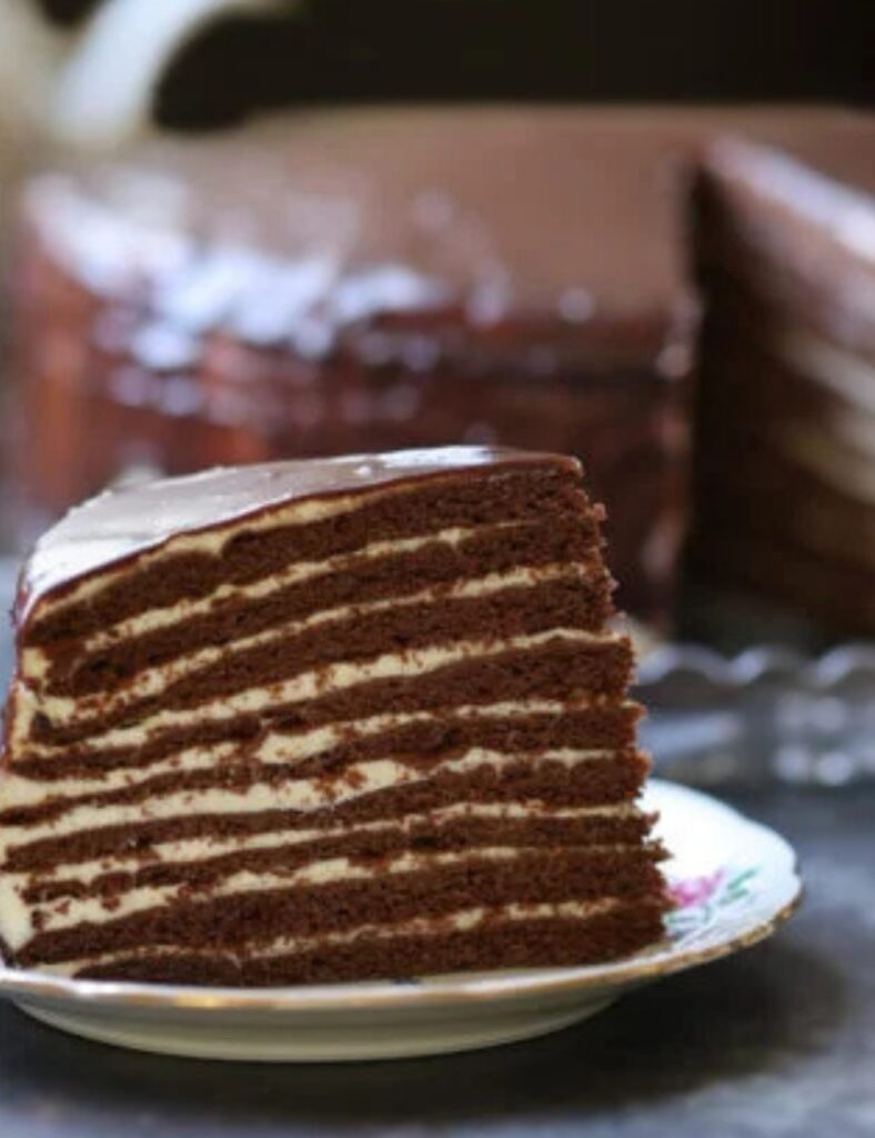 A slice of rich chocolate cake on a white plate, garnished with a dusting of cocoa powder.

