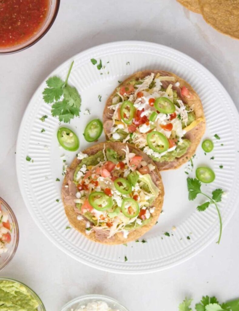 Two small tortillas topped with seasoned chicken and colorful vegetables, arranged neatly on a plate.