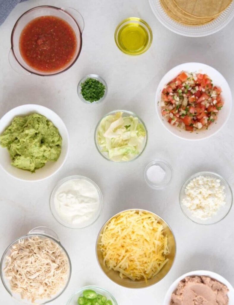Taco salad ingredients, including lettuce, tomatoes, cheese, and salsa, are neatly arranged on a table.