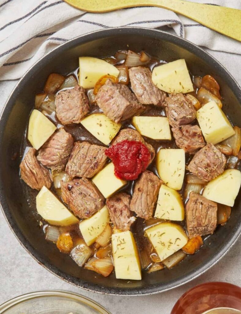 A frying pan containing raw meat and a pat of butter and potato , ready for cooking.

