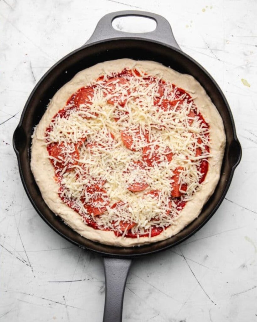 A pizza in a cast iron skillet topped with melted cheese and rich tomato sauce.