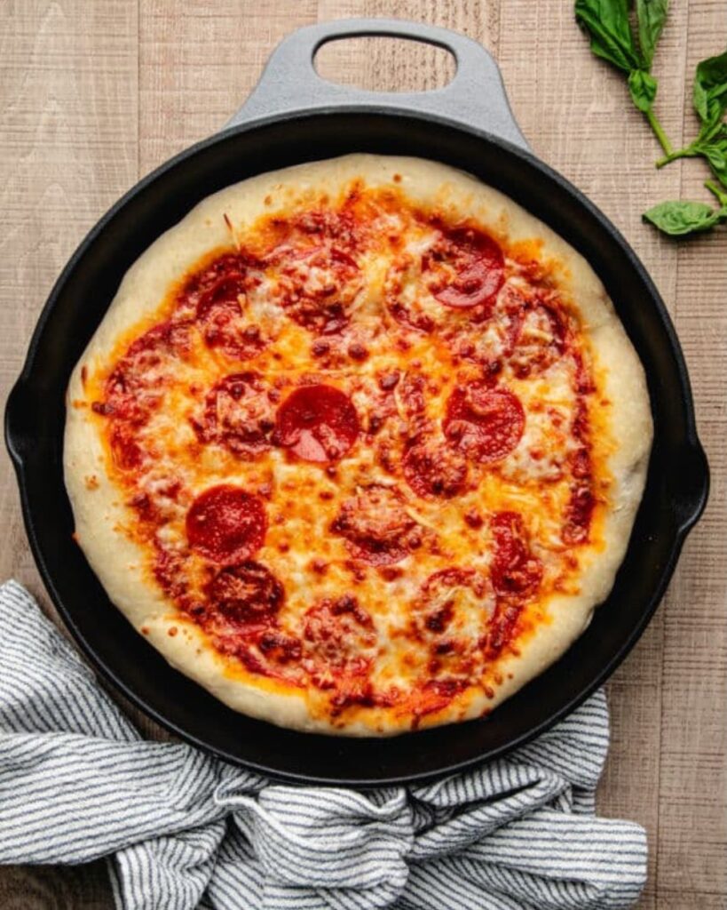 A pizza in a cast iron skillet rests on a rustic wooden table, showcasing its golden crust and melted cheese.