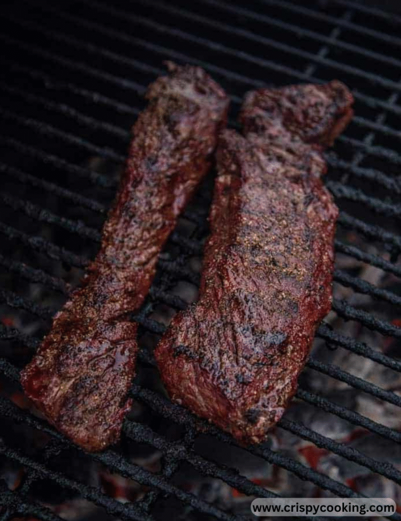 Two juicy steaks sizzling on a grill against a black background.