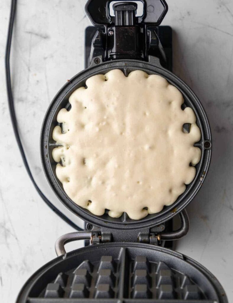 Waffle maker with a golden-brown waffle inside, showcasing its textured surface and steam rising from the appliance.