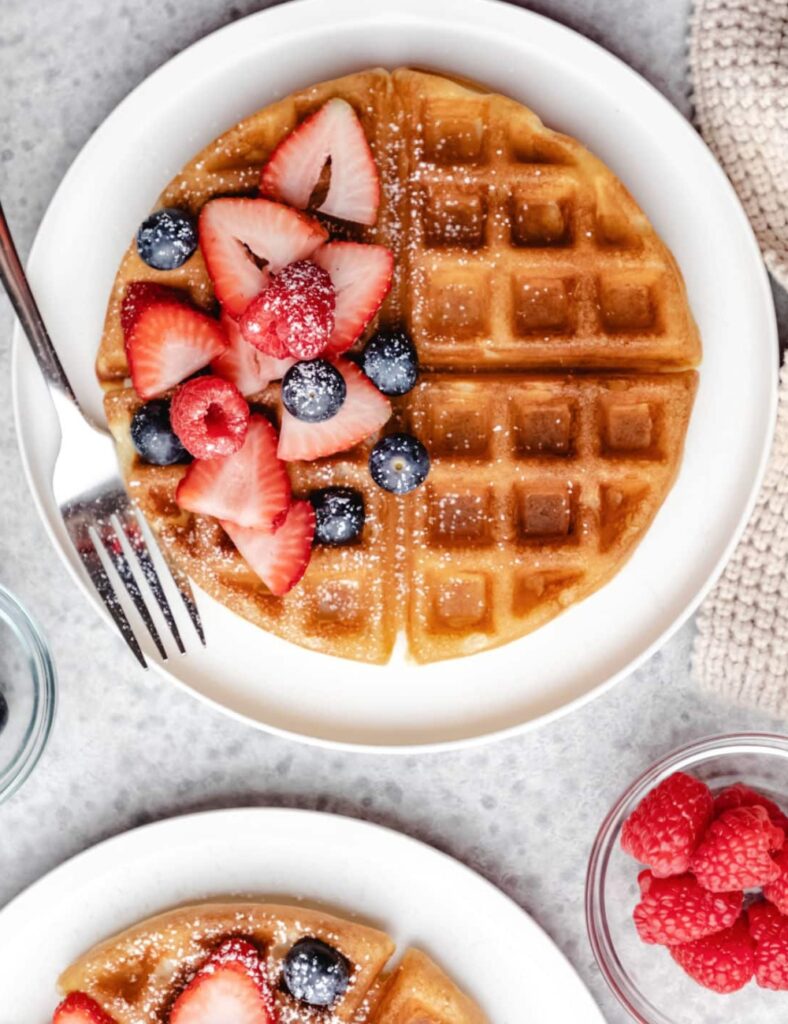 Waffles topped with fresh berries and drizzled with maple syrup on a white plate.