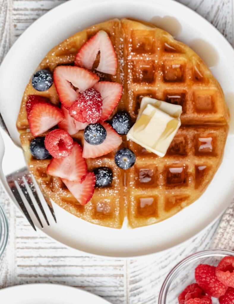 Waffles topped with fresh berries and a pat of butter, served on a white plate.