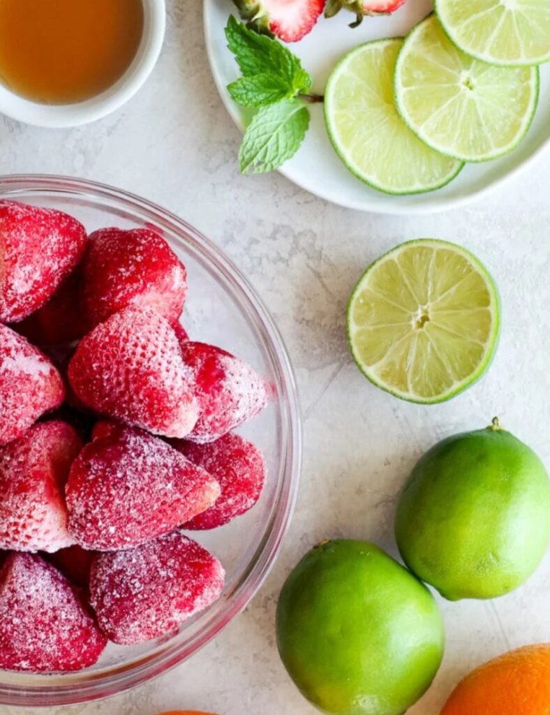 Fresh strawberries, lime, and orange slices artfully arranged on a wooden table, showcasing vibrant colors and textures.