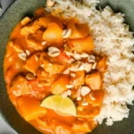 A bowl of Chicken Massaman Curry served with rice and garnished with herbs.