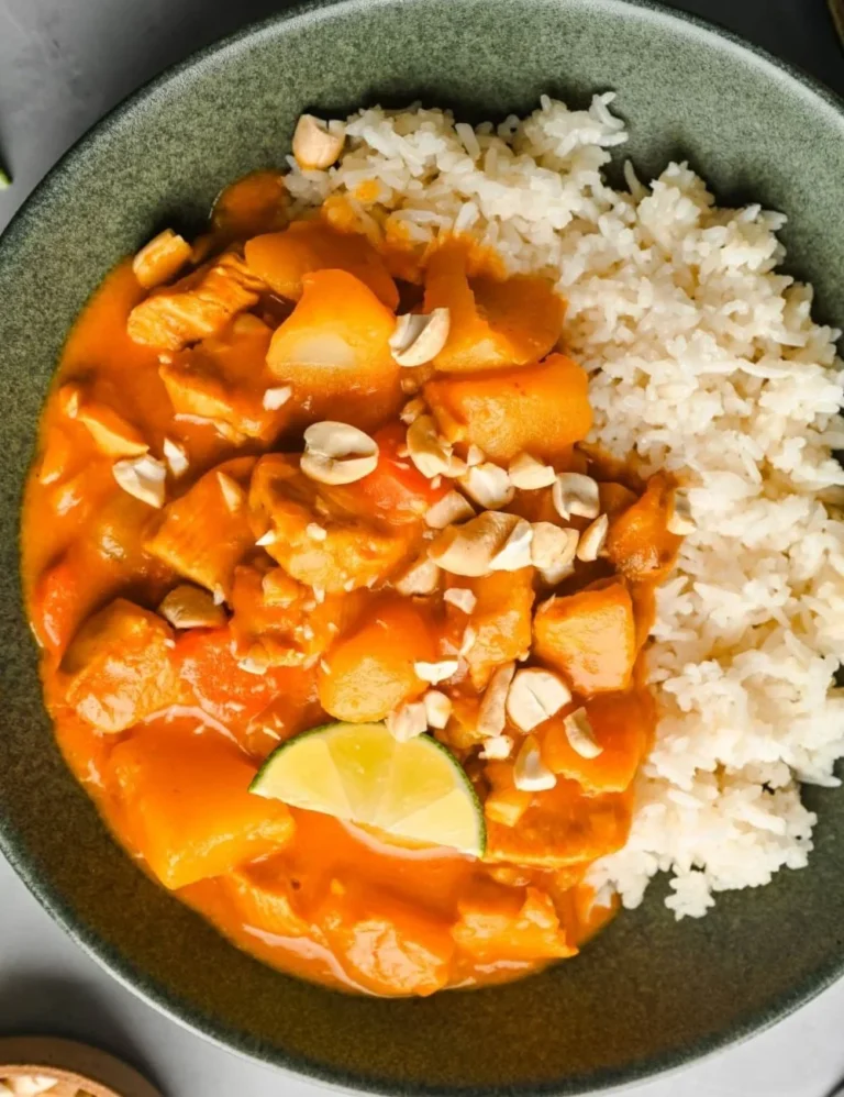 A bowl of Chicken Massaman Curry served with rice and garnished with herbs.