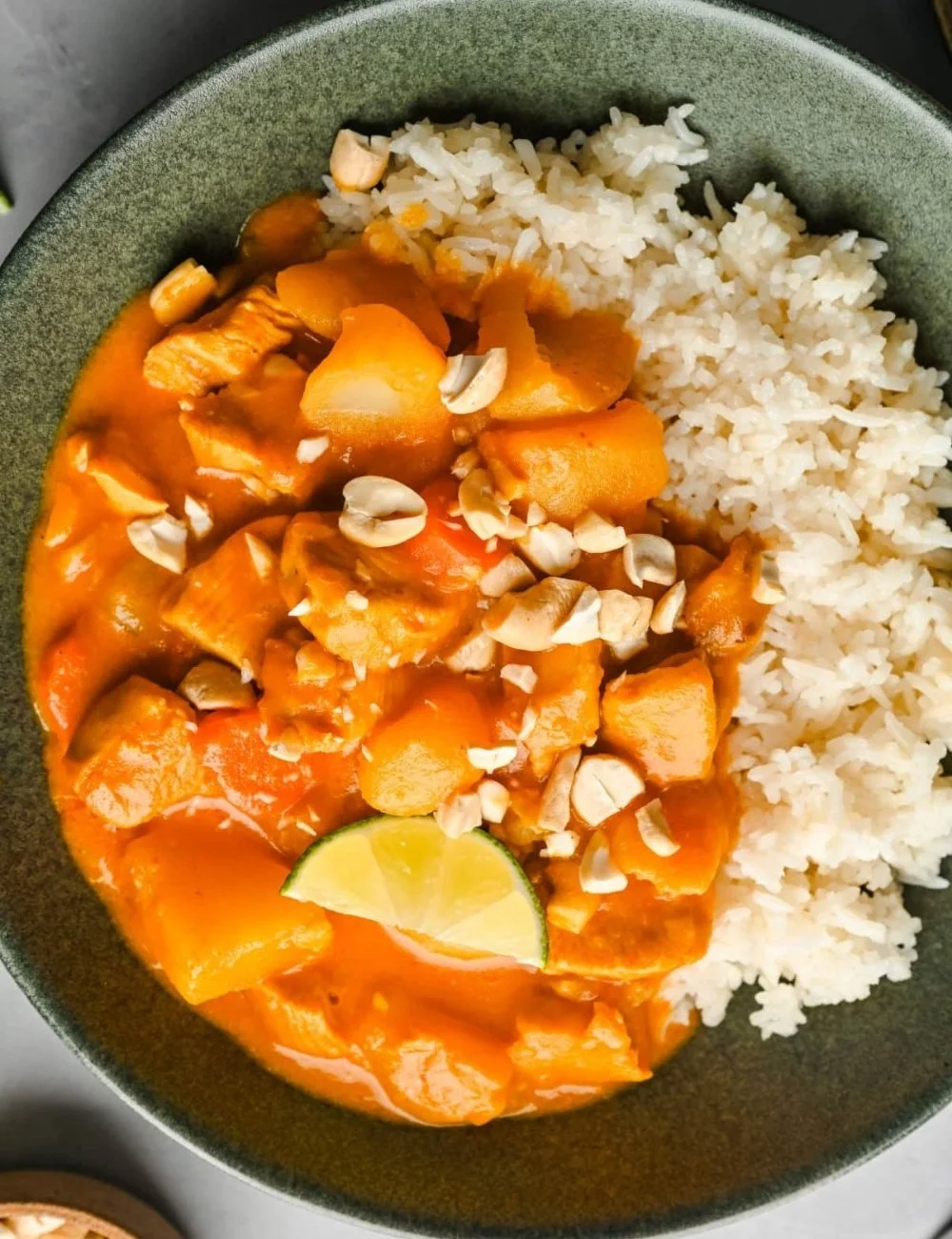 A bowl of Chicken Massaman Curry served with rice and garnished with herbs.