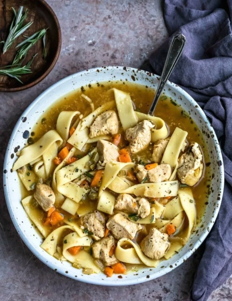 A bowl of hearty chicken noodle soup with fresh vegetables and herbs