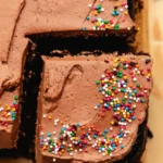 Delicious chocolate sheet cake topped with frosting on a rustic wooden table.
