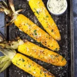 Grilled corn on the cob served on a plate with spices and herbs.