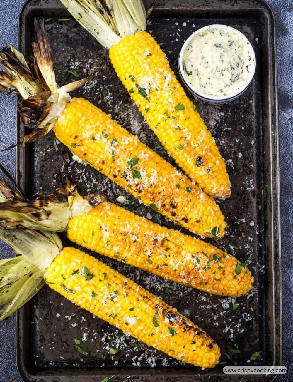 Grilled corn on the cob served on a plate with spices and herbs.