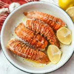 Grilled lobster tail served on a plate with lemon and herbs