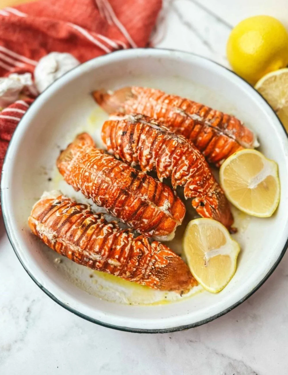 Grilled lobster tail served on a plate with lemon and herbs