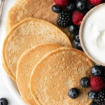 Delicious protein pancakes stacked on a plate with fresh berries and syrup.