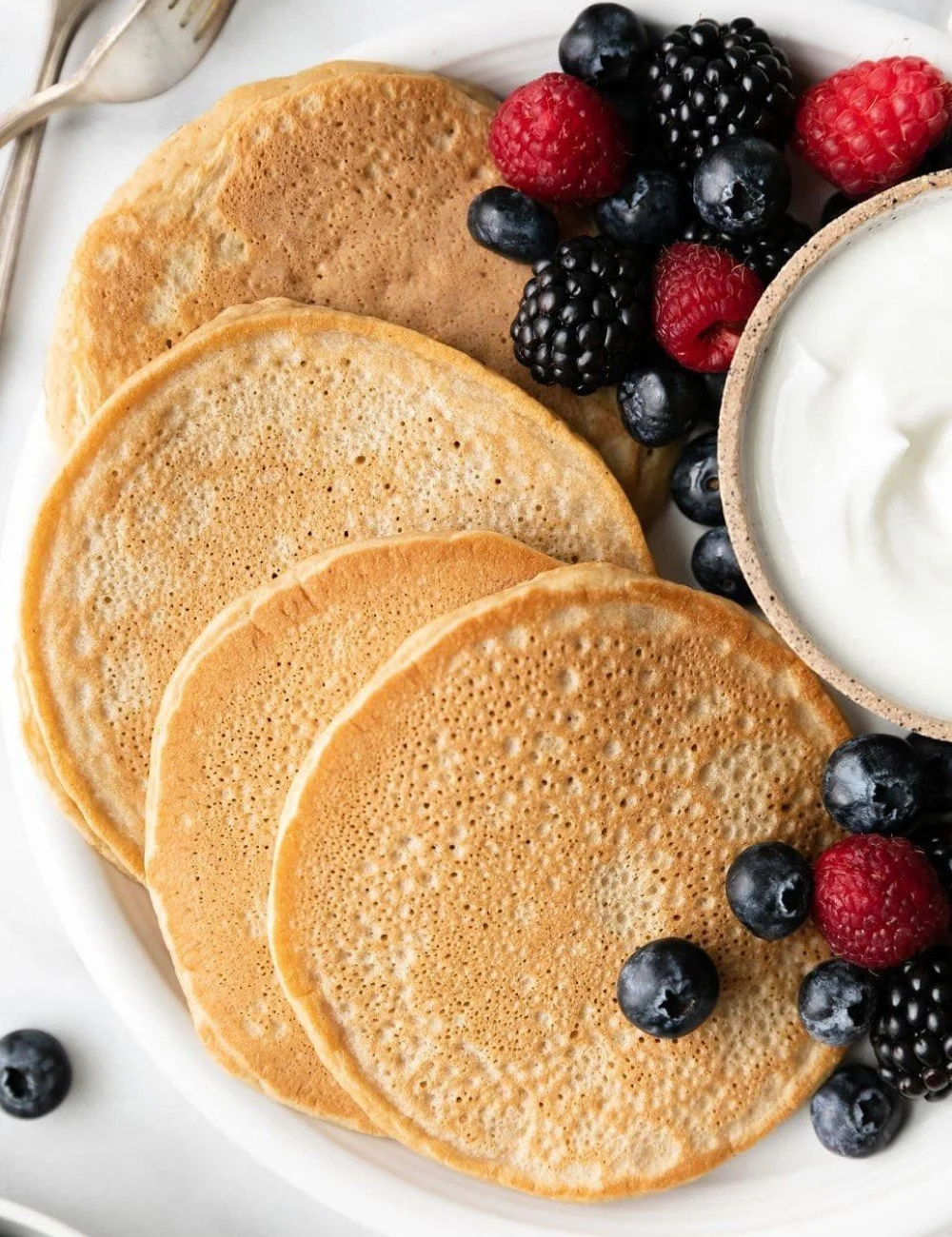 Delicious protein pancakes stacked on a plate with fresh berries and syrup.