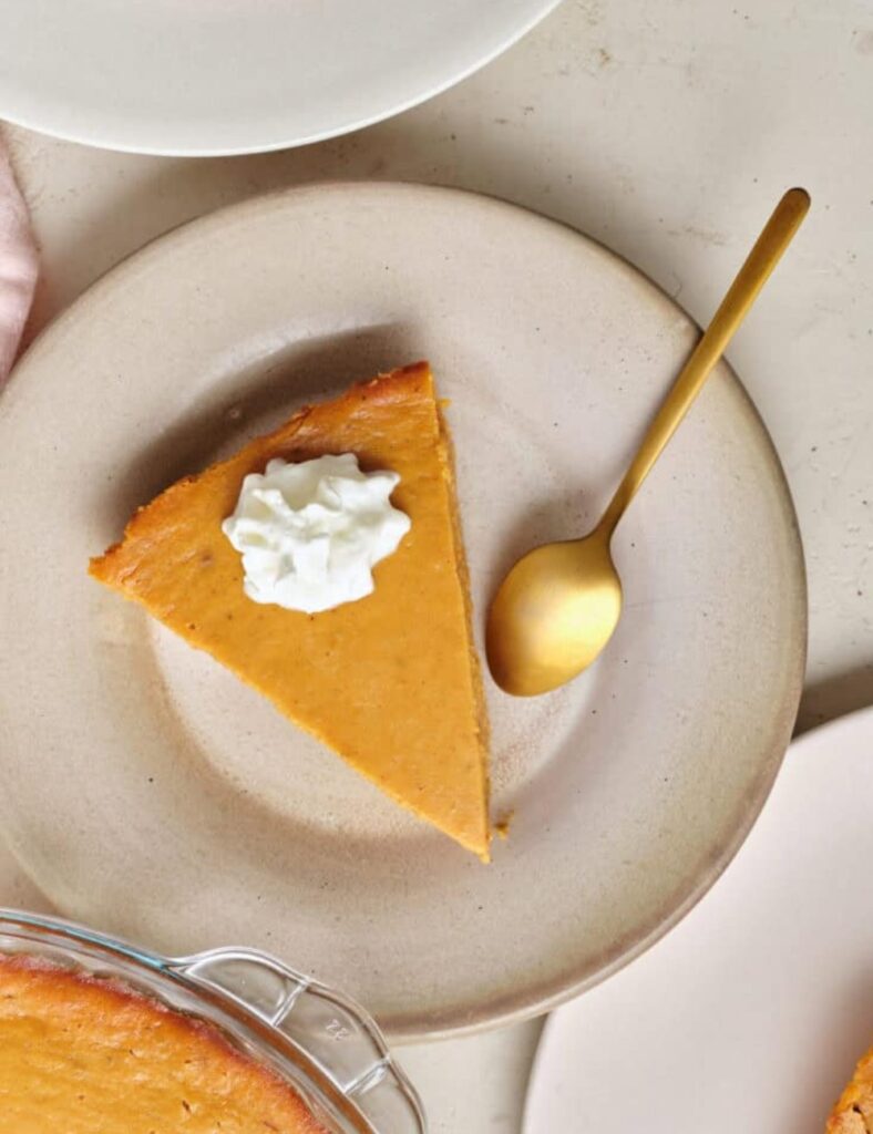  A slice of pumpkin pie topped with a dollop of whipped cream on a white plate.