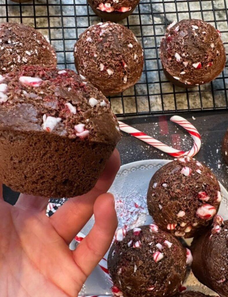 A person holds a chocolate muffin topped with candy canes, showcasing a festive and delicious treat.

