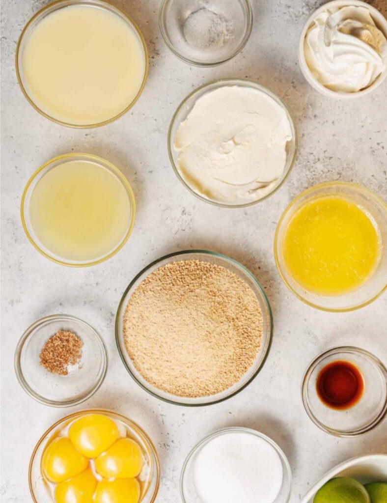Various cake ingredients arranged in bowls on a wooden table, including flour, sugar, eggs, and butter.