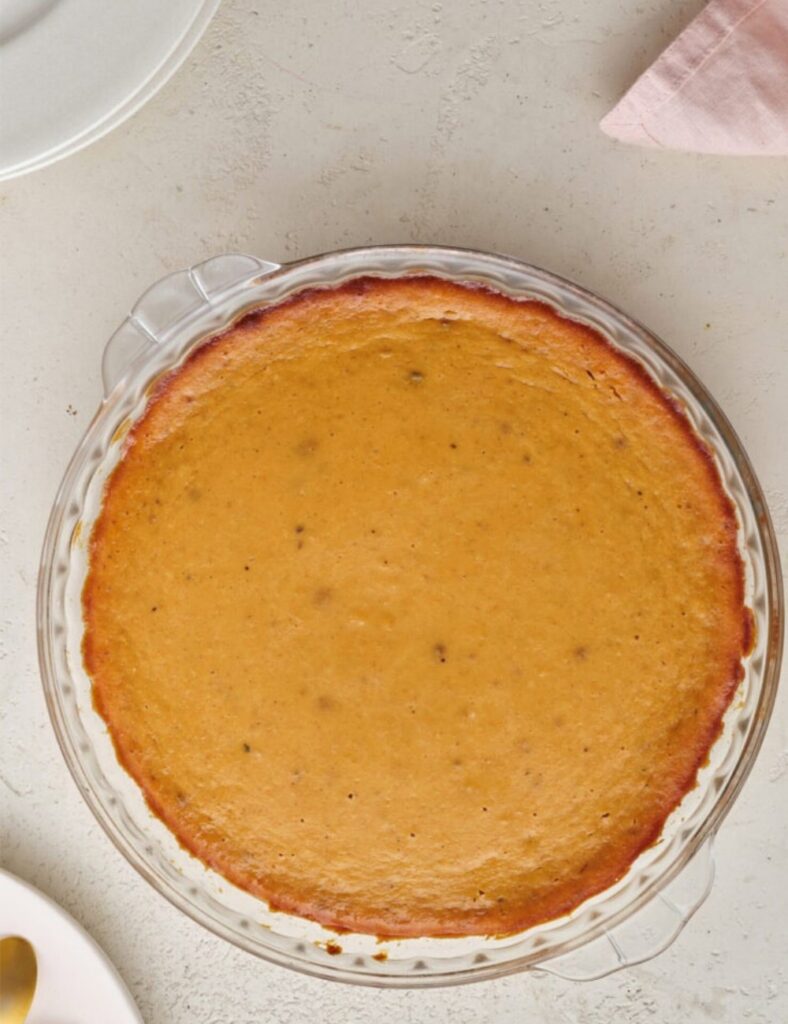 A freshly baked pumpkin pie in a clear glass pie dish, showcasing its golden crust and smooth, spiced filling.
