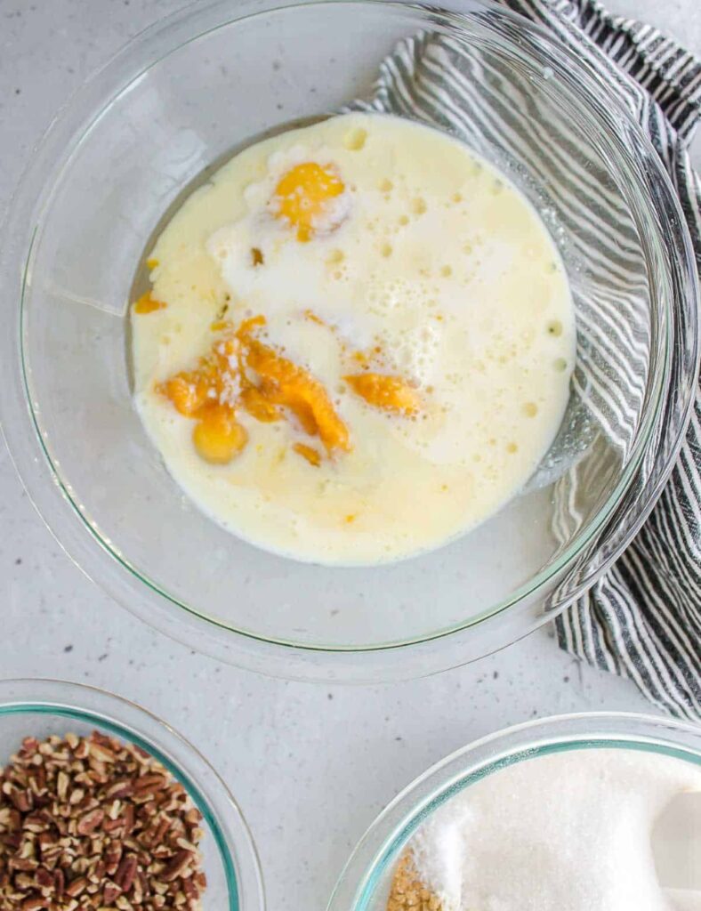 A bowl filled with fresh ingredients for peach cobbler, including sliced peaches, sugar, and flour.