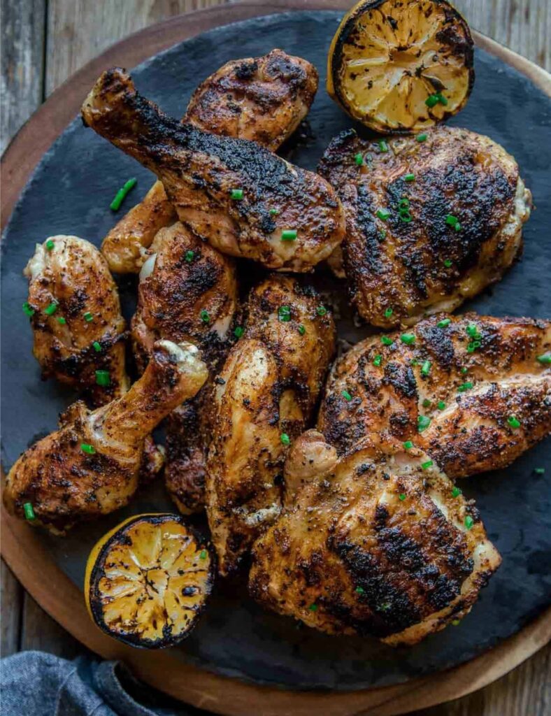 Grilled chicken served with lemon wedges on a sleek black plate, highlighting a delicious meal presentation.