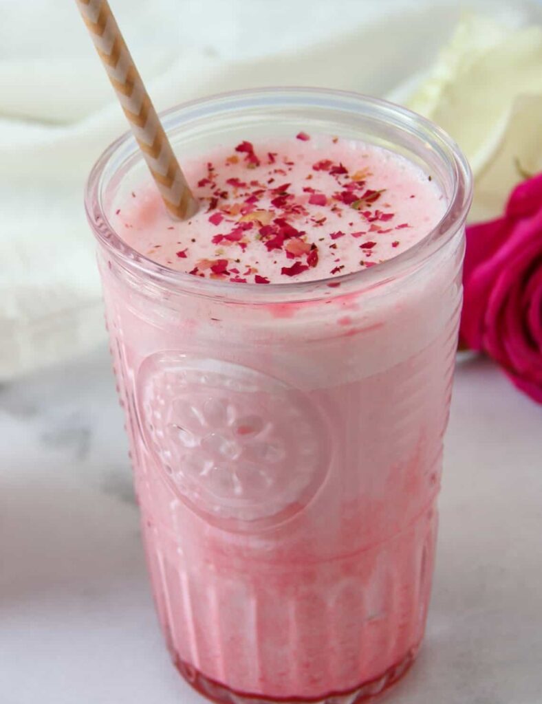 Two glasses of pink smoothie garnished with fresh strawberries and delicate rose petals.
