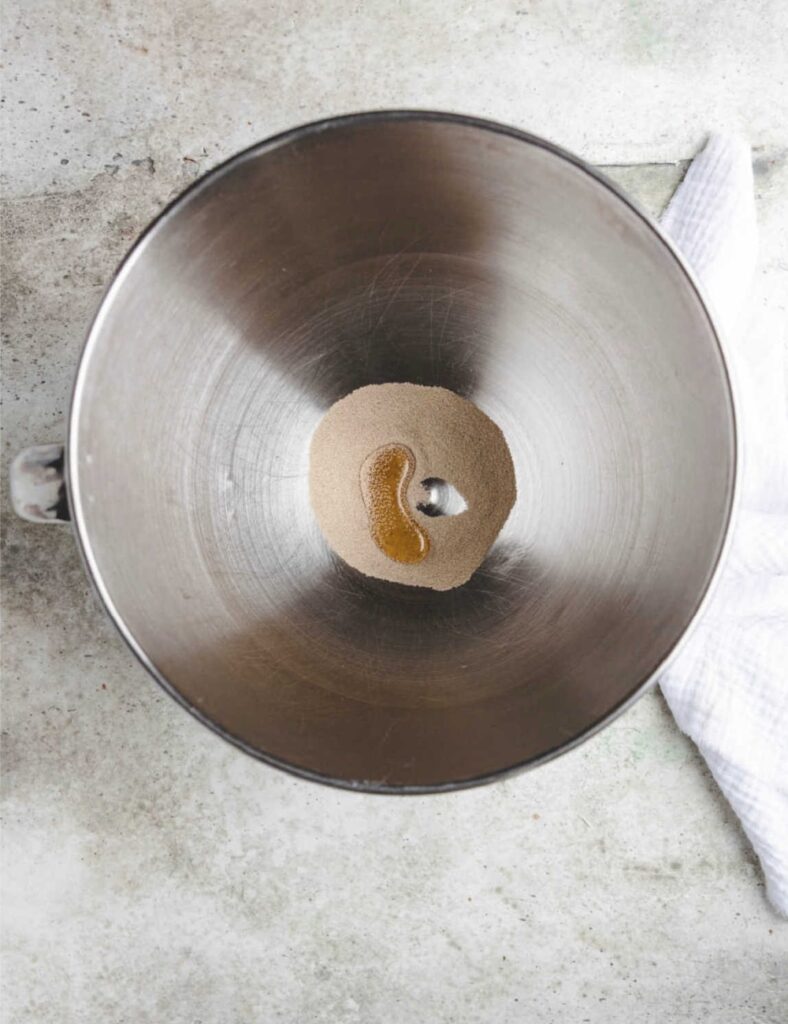 A metal bowl filled with liquid sits next to a folded white towel on a flat surface.