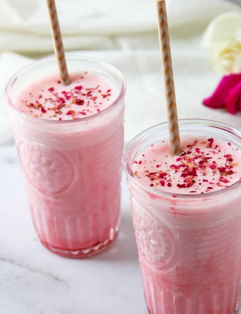  Two pink smoothies topped with strawberries and rose petals, served in clear glasses.