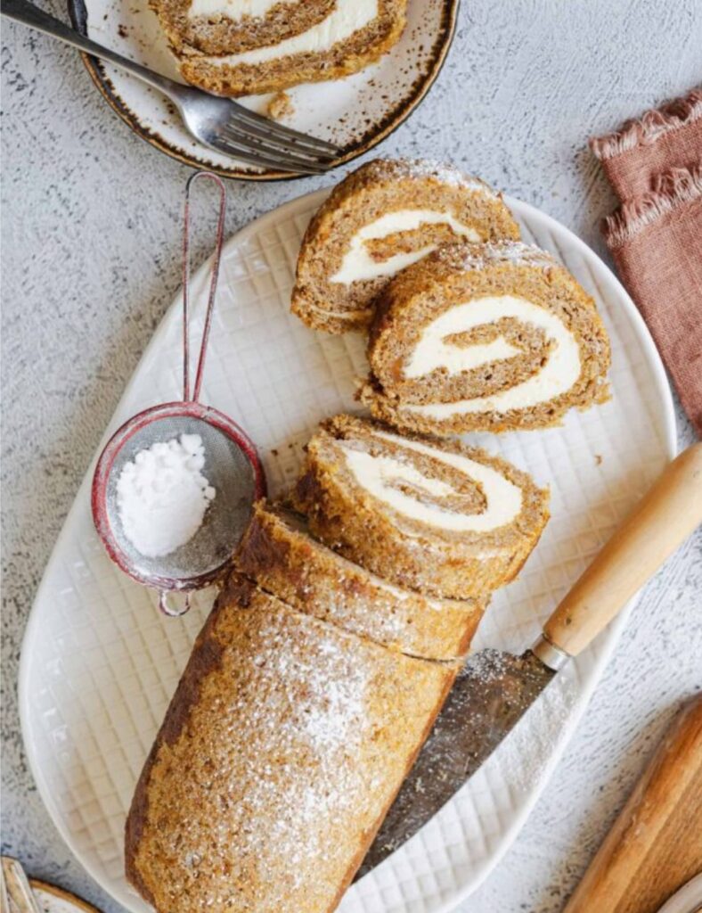 Pumpkin roll cake filled with cream cheese frosting, elegantly swirled and dusted with powdered sugar on a white plate.

