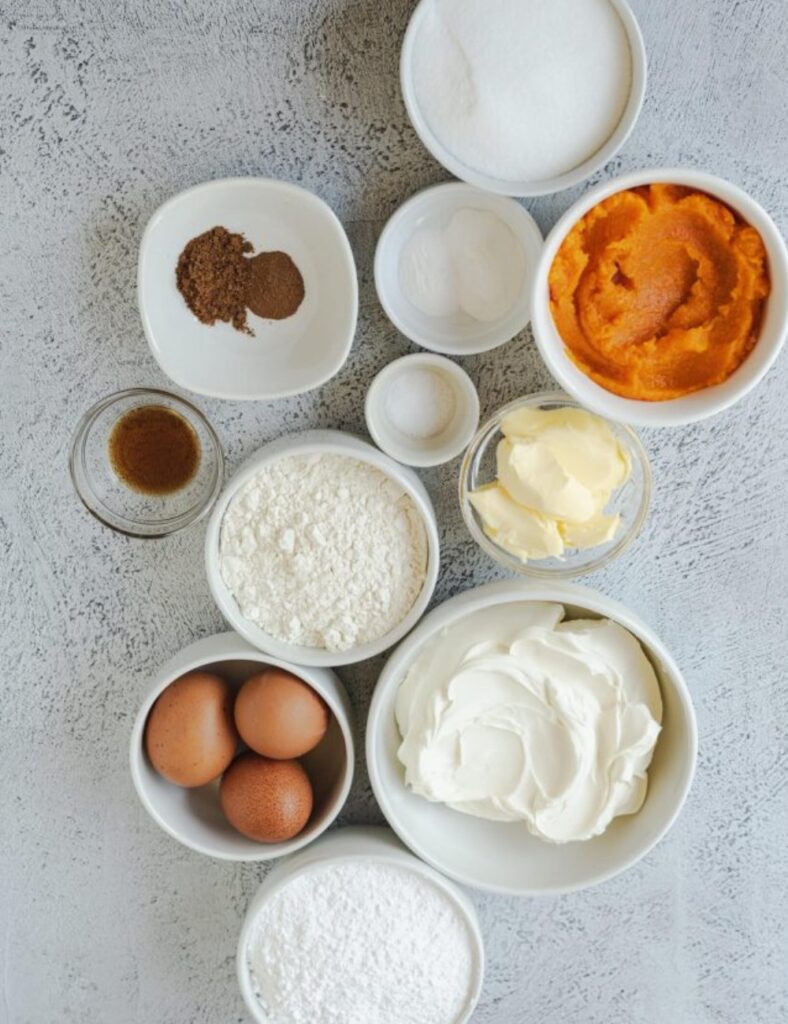Ingredients for pumpkin pie arranged in bowls, including pumpkin puree, spices, sugar, and pie crust.
