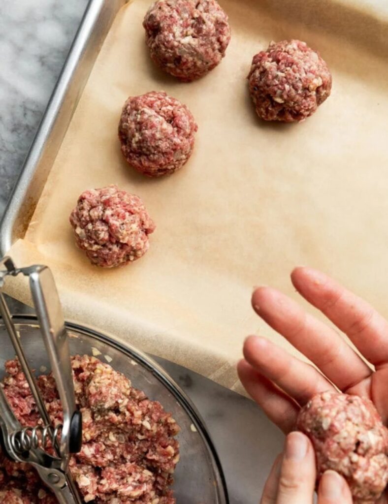 A person holding a meatball in their hand, showcasing the food item clearly against a neutral background.

