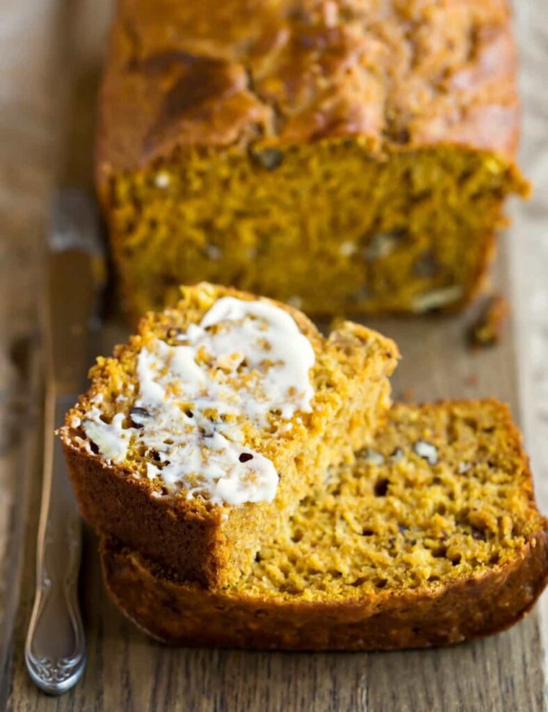  A loaf of pumpkin bread with a pat of butter sits on a wooden cutting board, ready to be served.