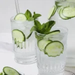 A refreshing glass of cucumber water with slices of cucumber and mint leaves.